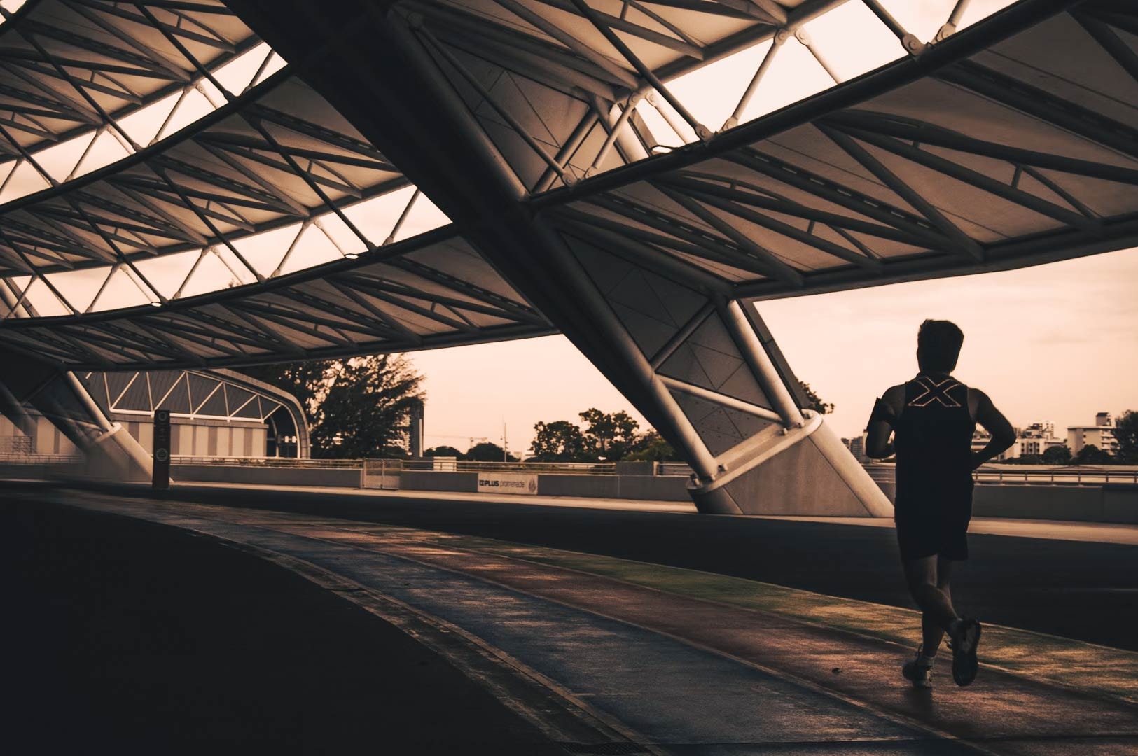 Person running on a covered outdoor track at sunrise, beneath a modern geometric roof structure.