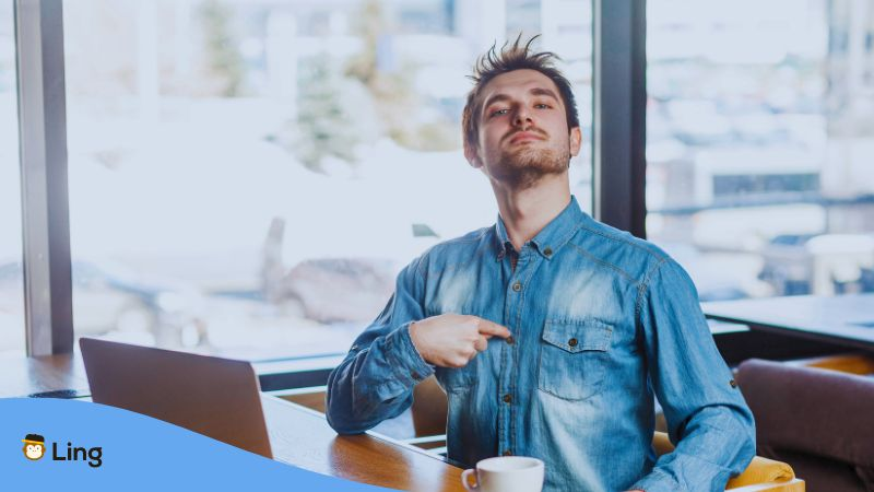 A photo of a man in front of a laptop pointing to himself.