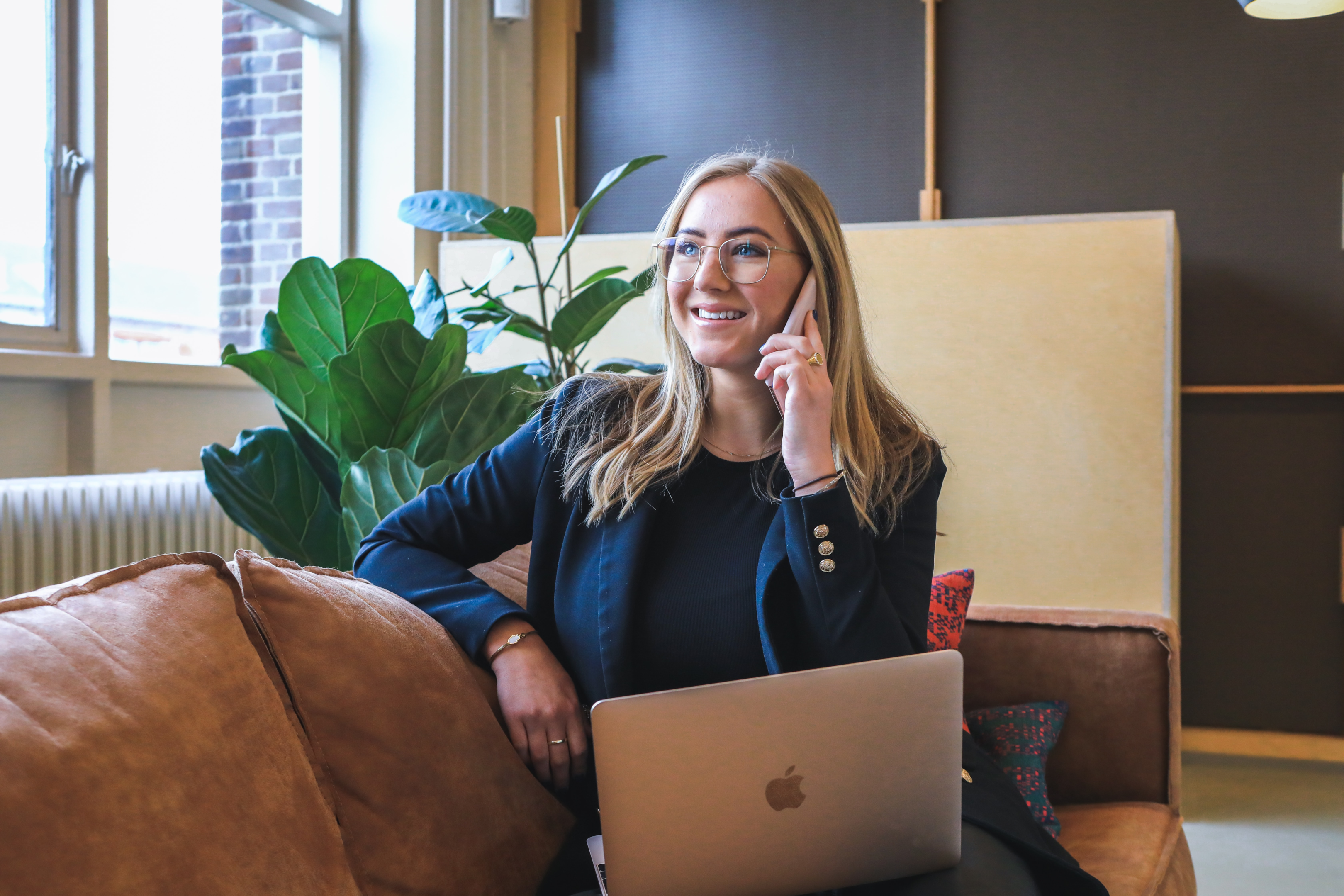5 Actions to Take When You Get a New Client | Brittany Corporation Photo of a woman wearing a blue suit and sitting on a leather sofa while taking a phone call.