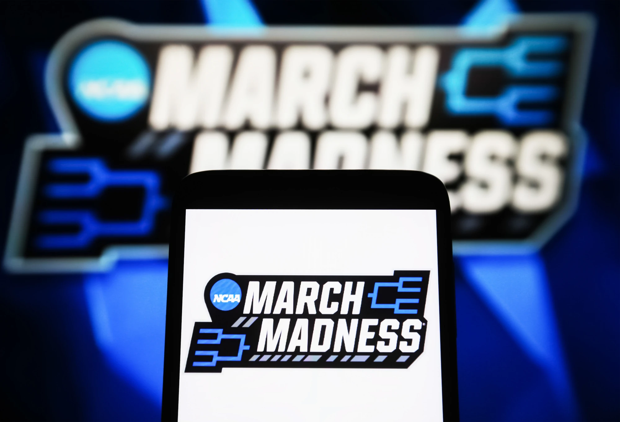 A March Madness (NCAA Division I men's basketball tournament) logo is seen on a smartphone and a PC screen. 