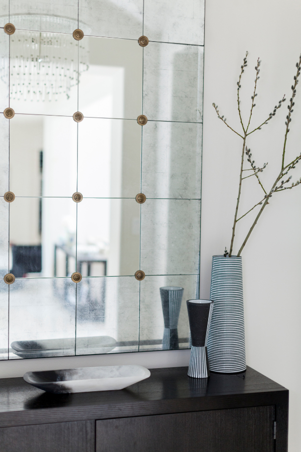 A console table with a large antiqued mirror and a small grouping of striped and sculptural ceramic vases, creating a minimal and refined vignette.