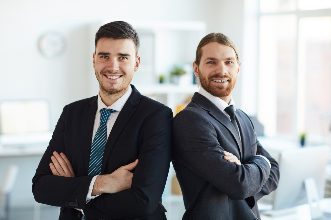 Two confident business brokers standing with arms crossed in a modern office
