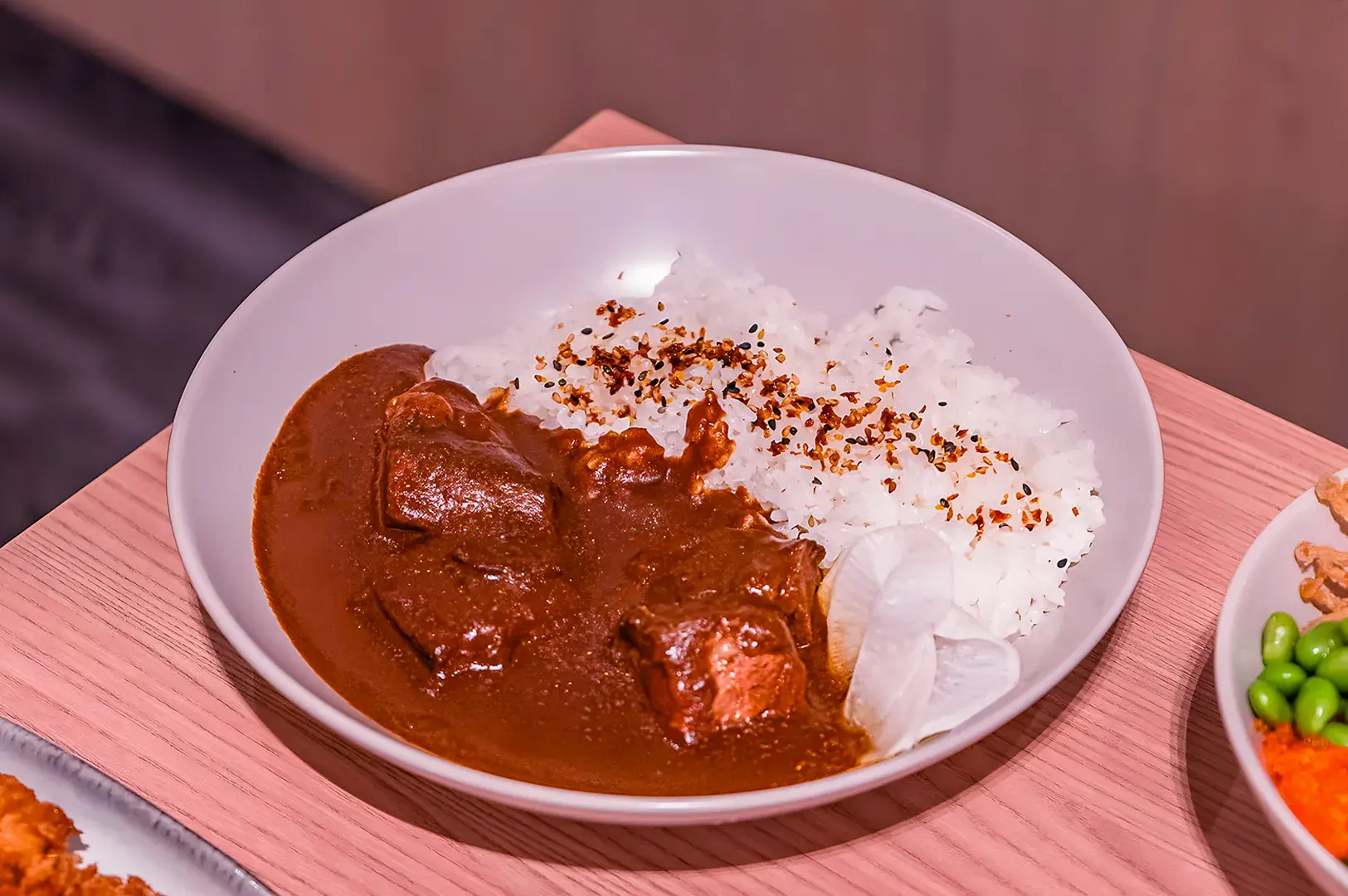 Close-up food photo of Japanese curry rice dishes featuring crispy chicken katsu, sliced beef, and omelet curry, served with rice, gyoza dumplings, and side sauces on a wooden table.