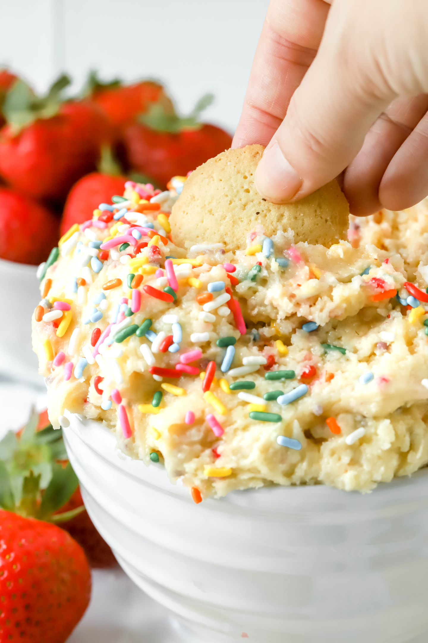 Nilla vanilla wafer being dipped into a bowl of Funfetti cake batter dip
