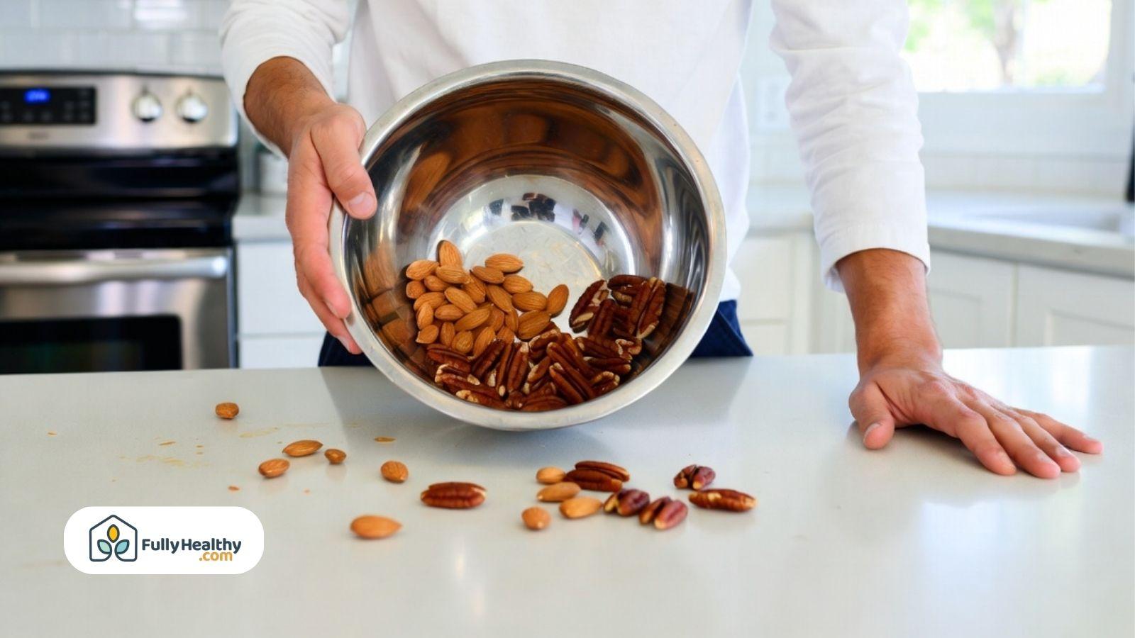 Person pouring mixed almonds and pecans from a metal bowl onto a kitchen counter.