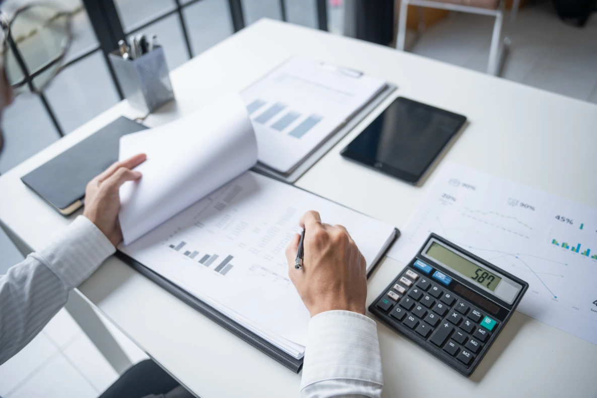 A close-up shot shows a calculator, a fountain pen, and a folder labeled "Finance" on a white surface.A close-up shot shows a calculator, a fountain pen, and a folder labeled "Finance" on a white surface.