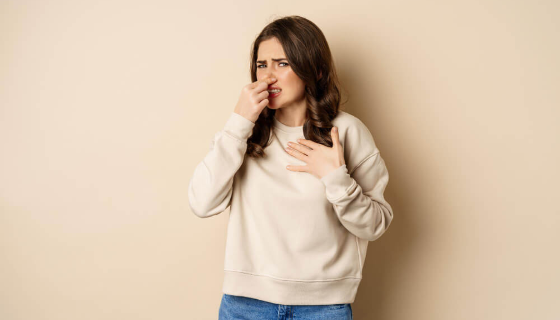 Kvinne holder for nesen med misfornøyd uttrykk, tegn på dårlig lukt eller ubehag relatert til pust eller munn.