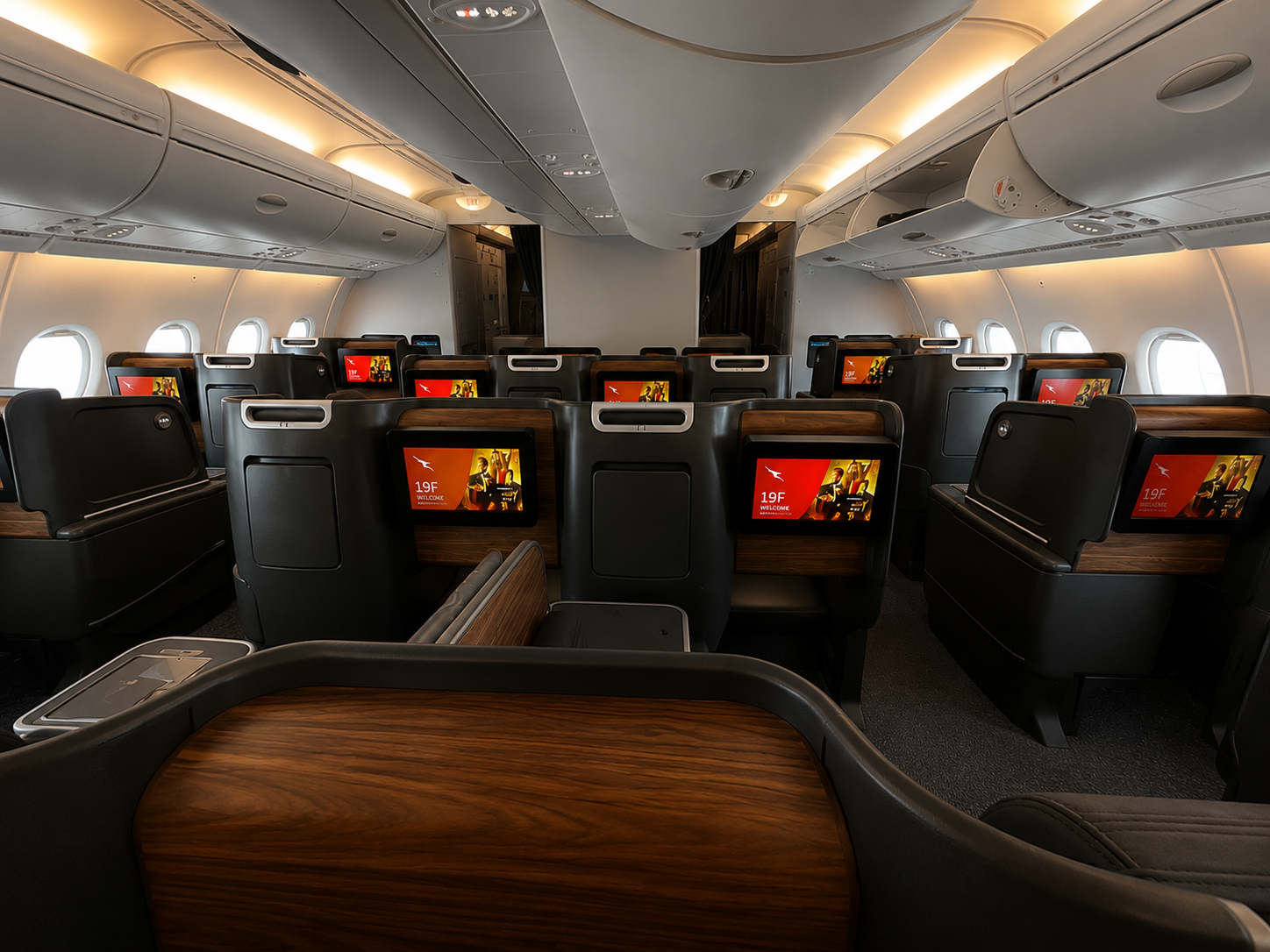 Qantas-style A380 business class cabin with empty lie-flat seats, wood accents, and individual entertainment screens.