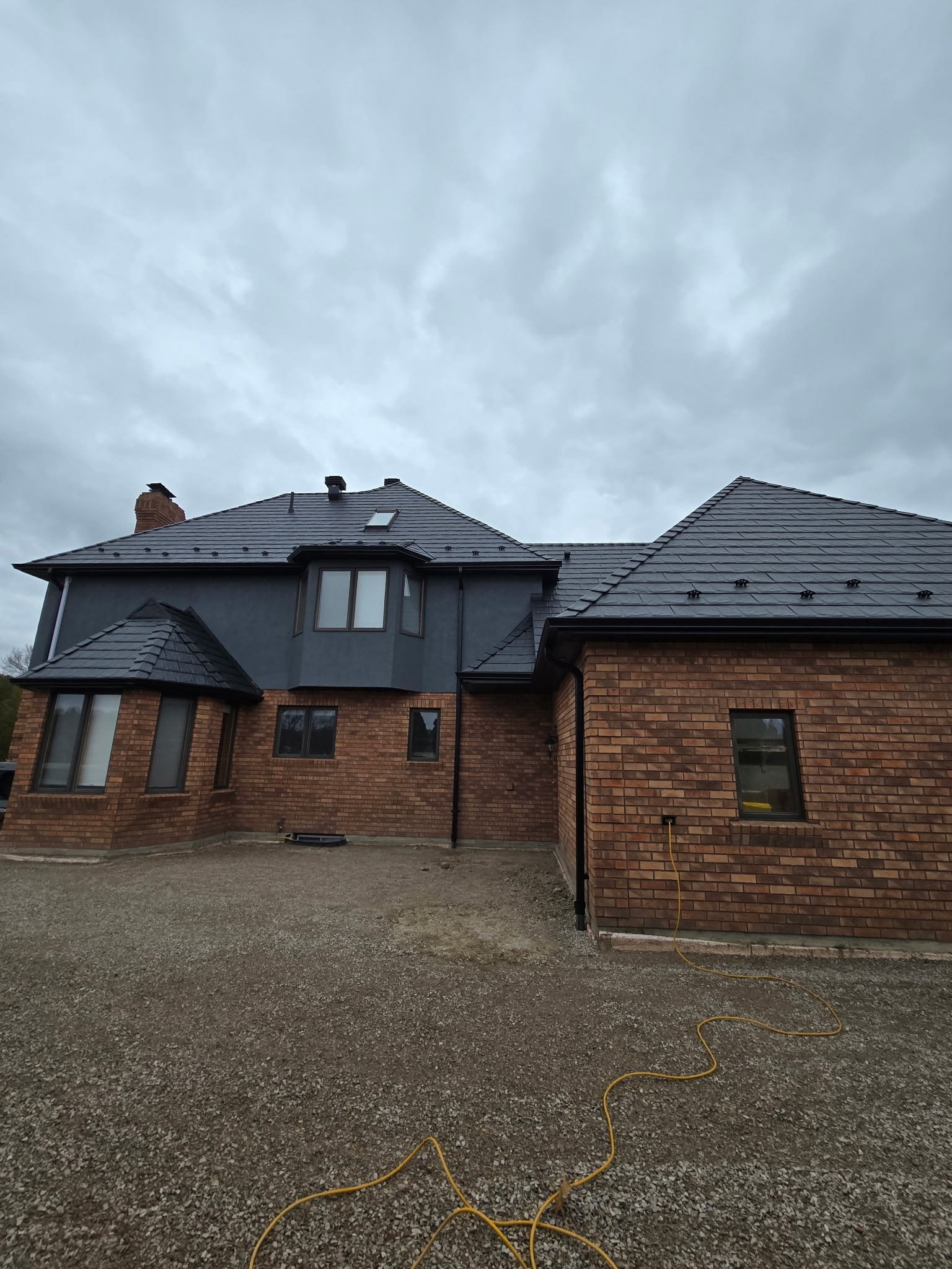 A house with a black metal roof, showcasing a driveway that extends to the entrance.