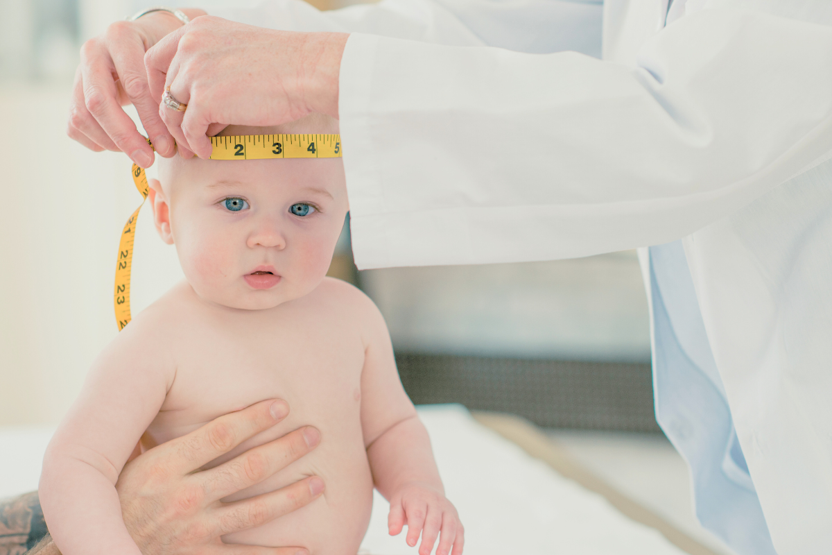 Doctor measures babies head while baby is sitting. Poppyseed Play