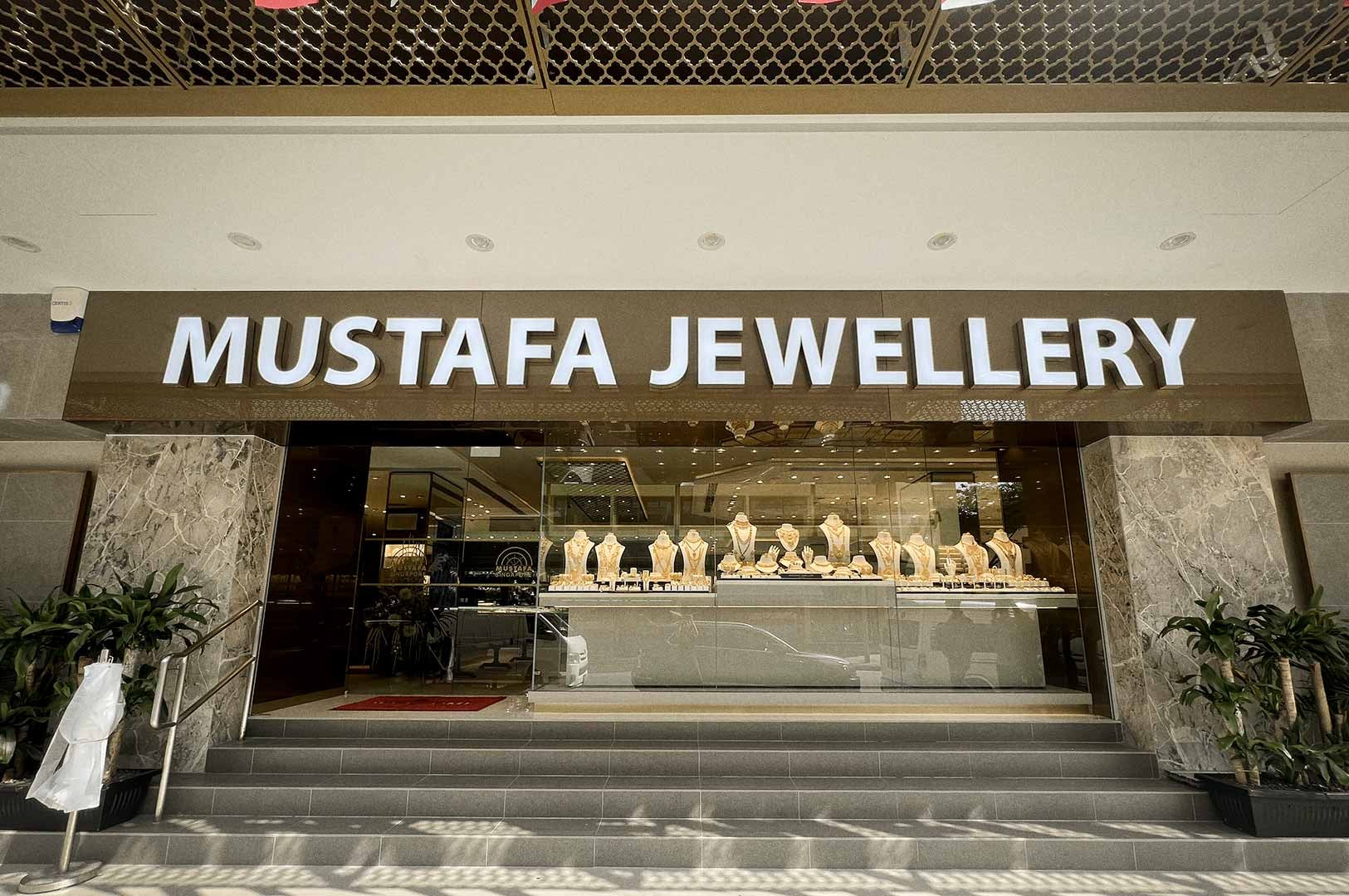 The storefront of Mustafa Jewellery featuring a bright sign above a glass display filled with gold necklaces and ornaments.