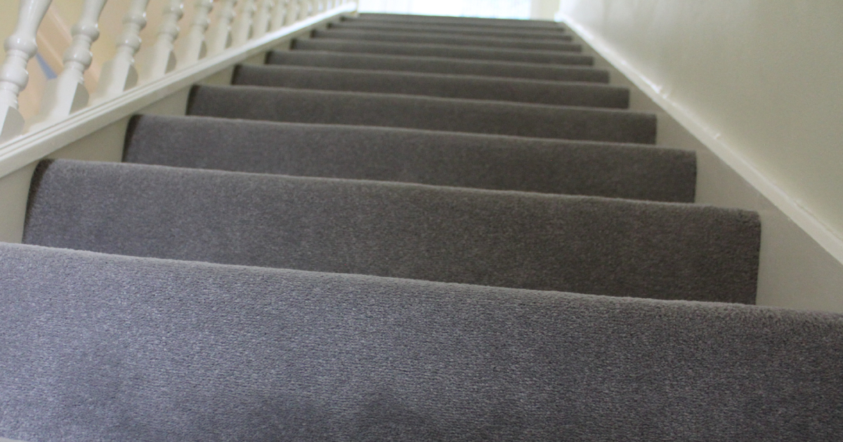 Een vernieuwde trap met grijs tapijt en een witte trapleuning.