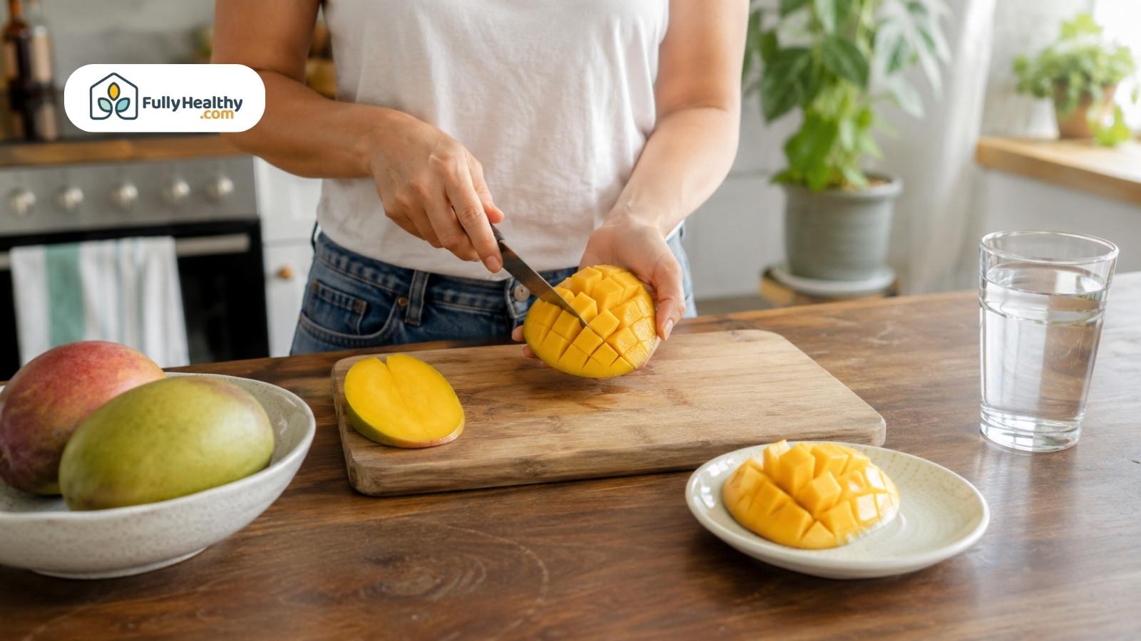 Person slicing ripe mango cheeks on wooden cutting board beside water glass