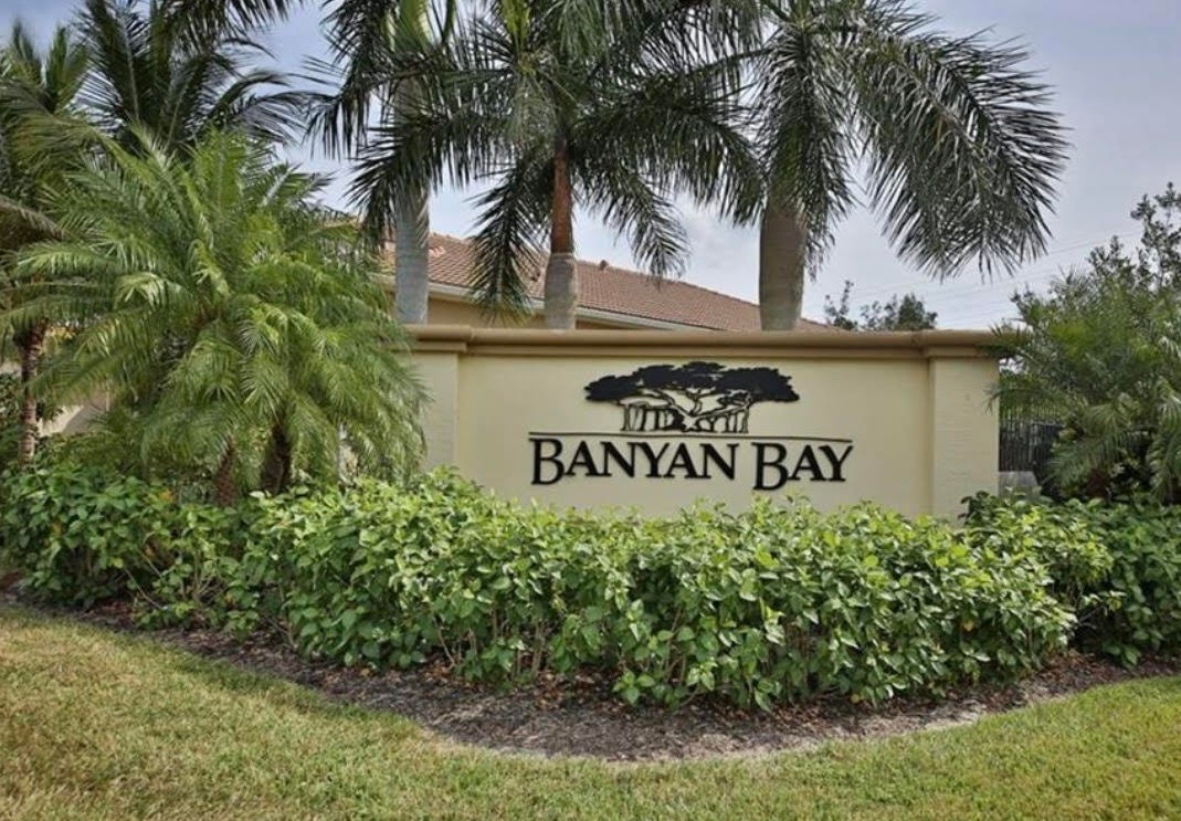 The image depicts the entrance of a gated community in Fort Myers, featuring a security gate surrounded by meticulously maintained landscaping. This serene setting offers residents a peaceful retreat with access to amenities like a sparkling community pool and nearby shopping centers.