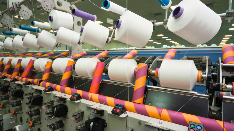 An industrial machine processes white thread spools using striped tubes, promoting sustainability and reducing waste.