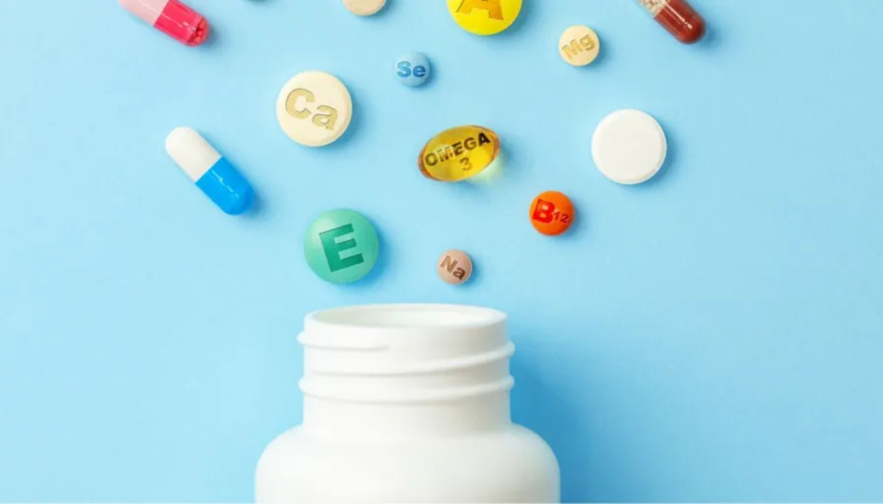 Fargerike vitaminer og mineraltilskudd svever over en åpen hvit pilleboks på blå bakgrunn, symboliserer ernæringsstøtte.