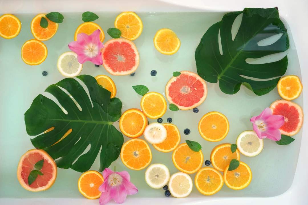 Fresh fruit slices and tropical leaves floating in a water bath, creating a vibrant, refreshing spa atmosphere.