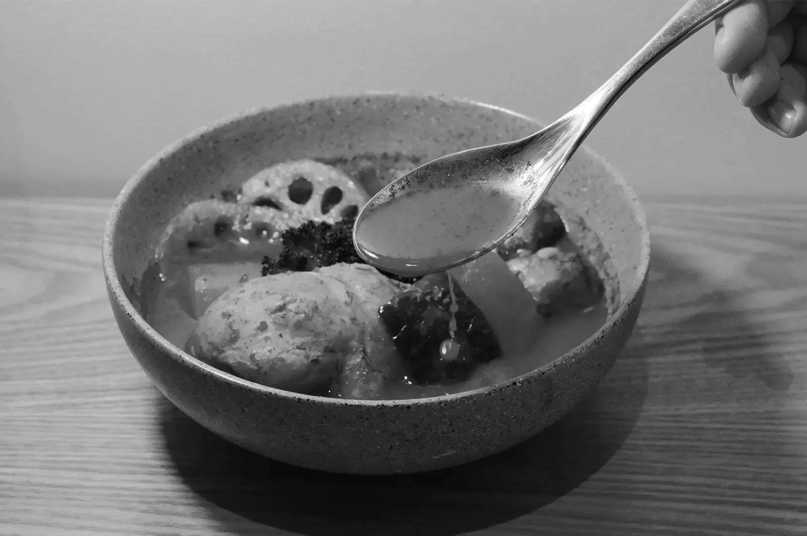 A close-up of Kisetsu soup curry in a ceramic bowl, filled with assorted ingredients in a savory broth, with a spoon held above the dish.