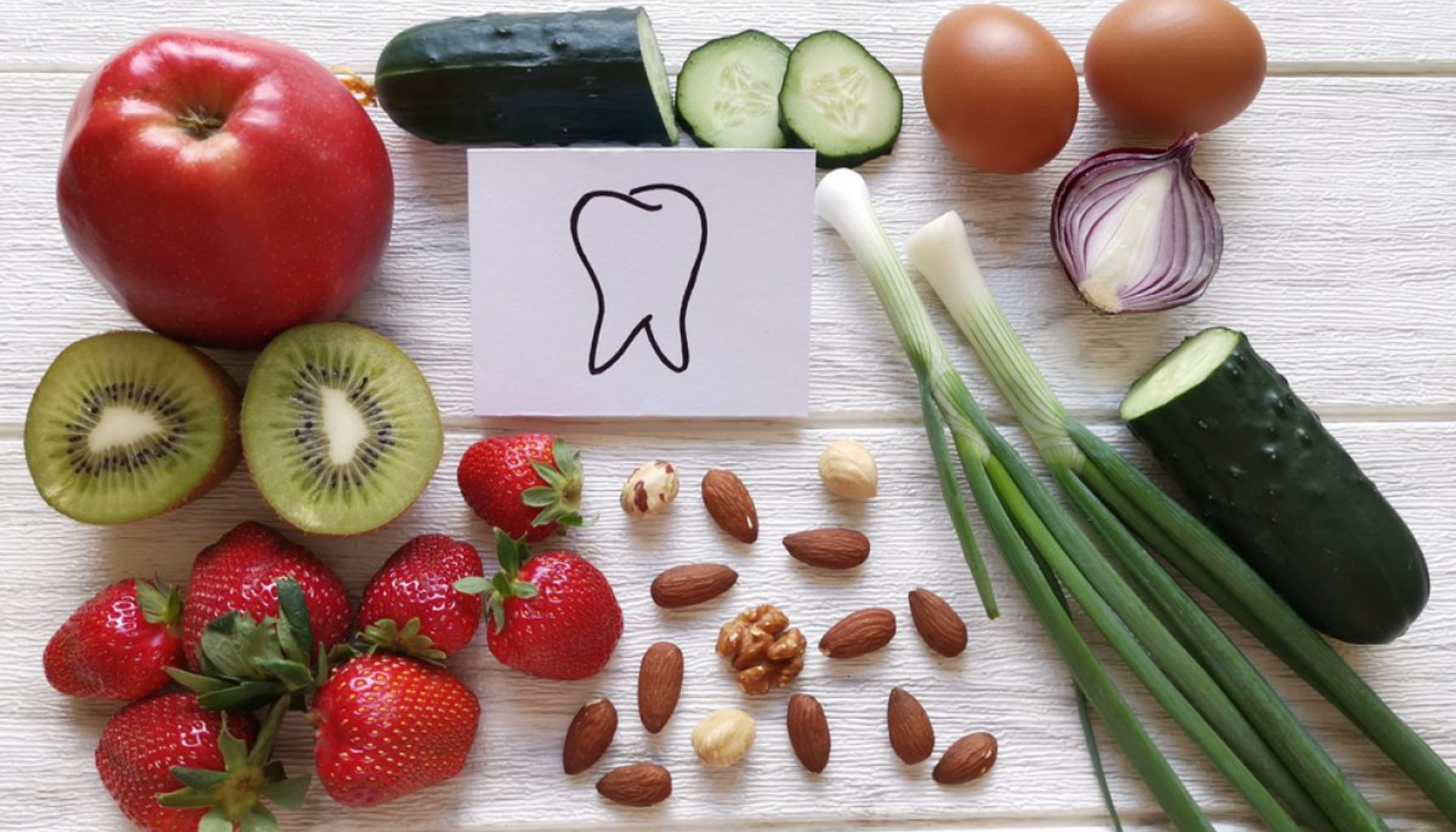Frukt, grønnsaker og nøtter rundt tegnet tann som viser mat for god tannhelse.
