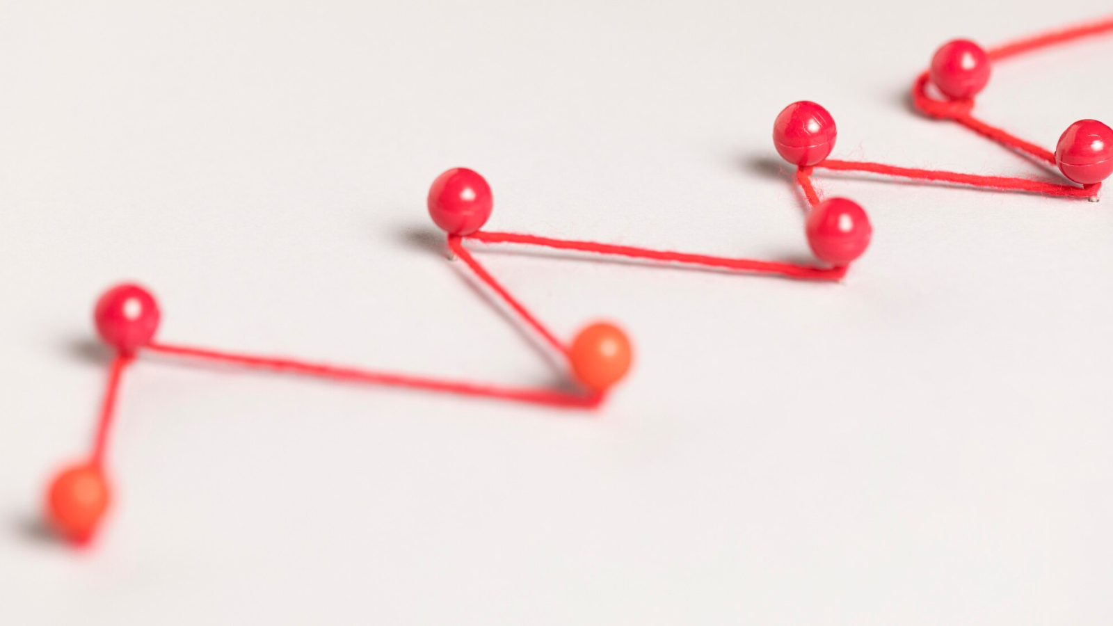 Red string connecting push pins in a zigzag pattern on a white surface, symbolizing a roadmap or step by step process.