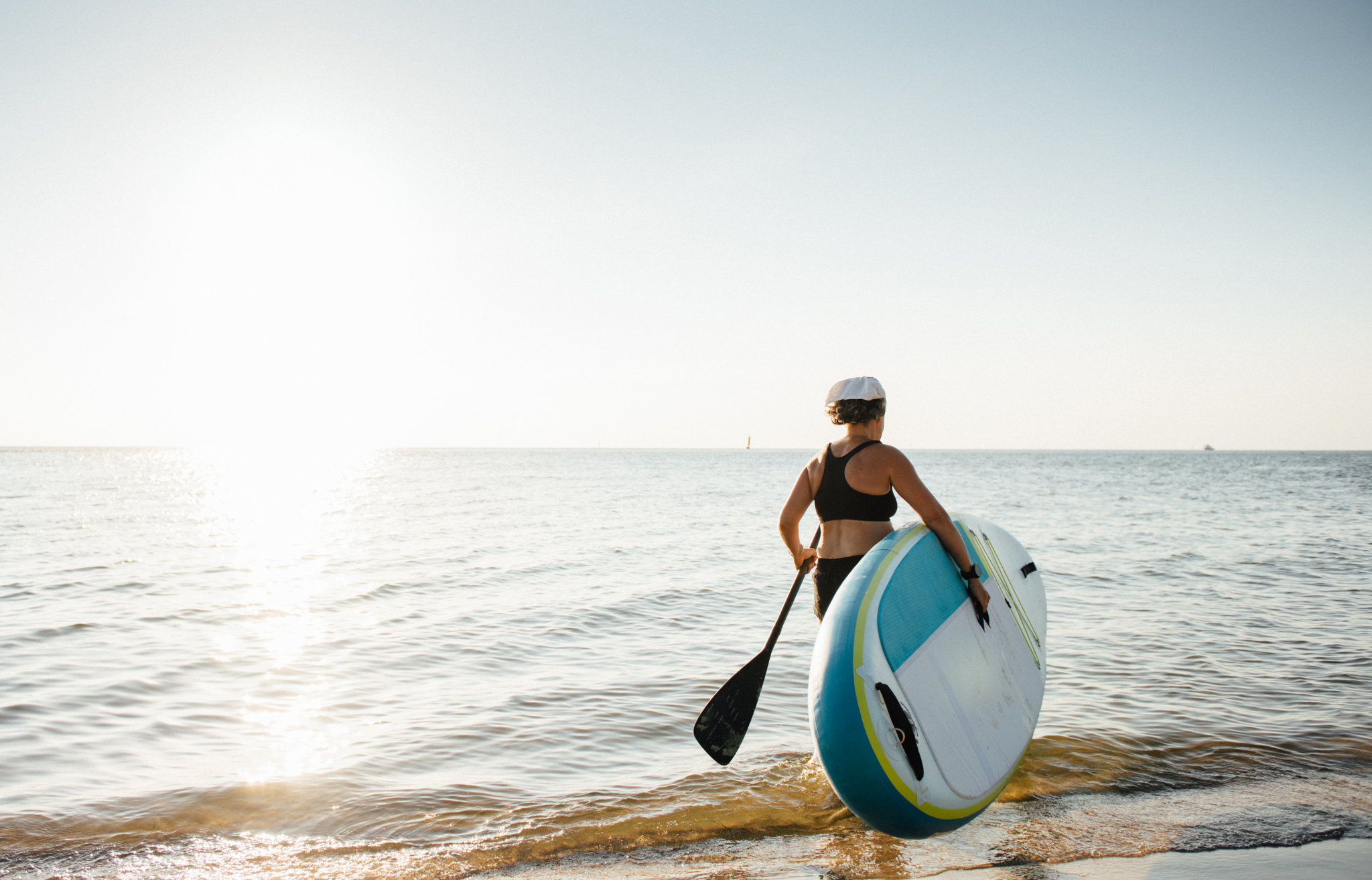 Woman carrying paddle board to water - Adventure Wise Travel Gear