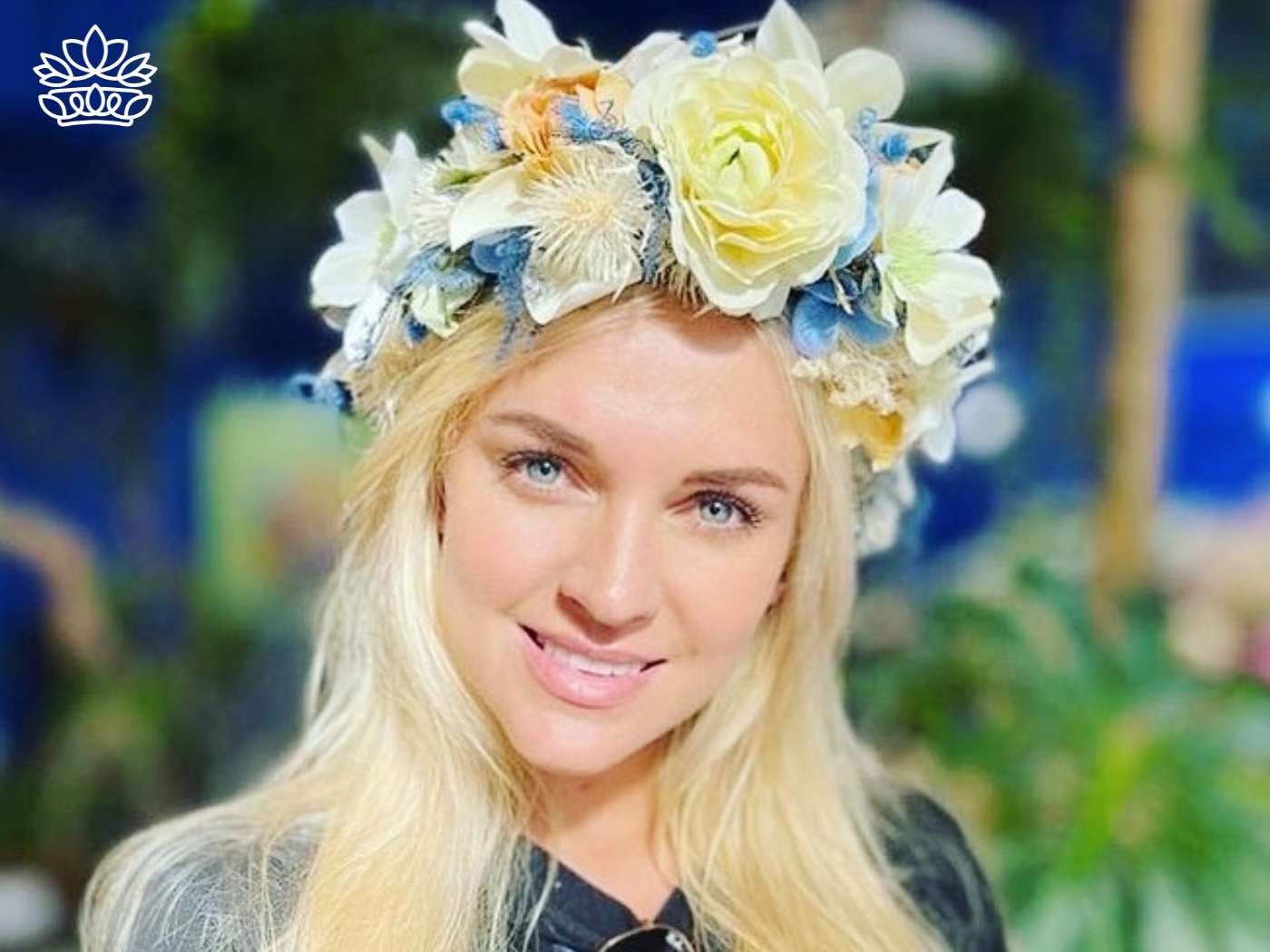 A woman with a warm smile wearing a flower crown of white and pale blue blooms, symbolizing freshness and elegance, from the exclusive range at Fabulous Flowers and Gifts.