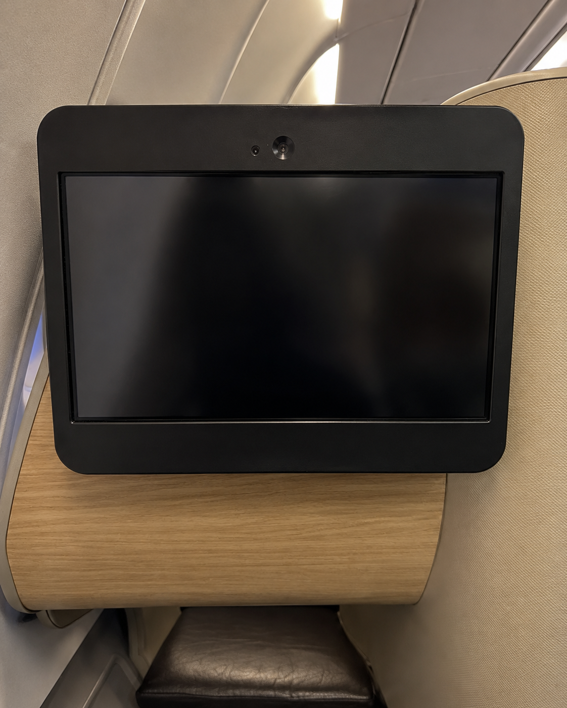 Business class entertainment screen turned off in a premium aircraft seat with wood trim and warm cabin lighting.
