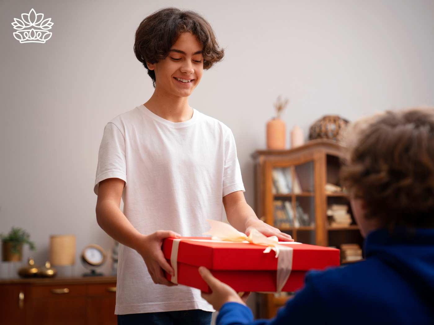 Smiling young boy giving a red gift box to another person, capturing a moment of joy and generosity, from the Gift Boxes by Type Collection at Fabulous Flowers and Gifts.