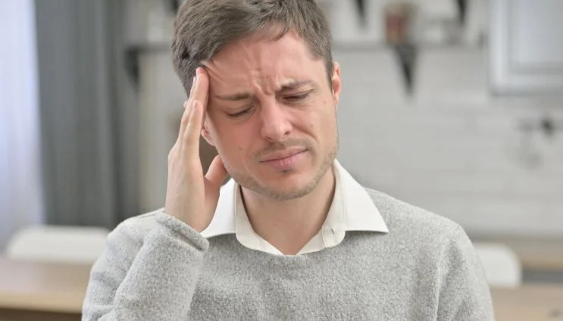 Mann holder seg til hodet og ser ut til å ha smerter, mulig hodepine eller svimmelhet i hjemmemiljø.
