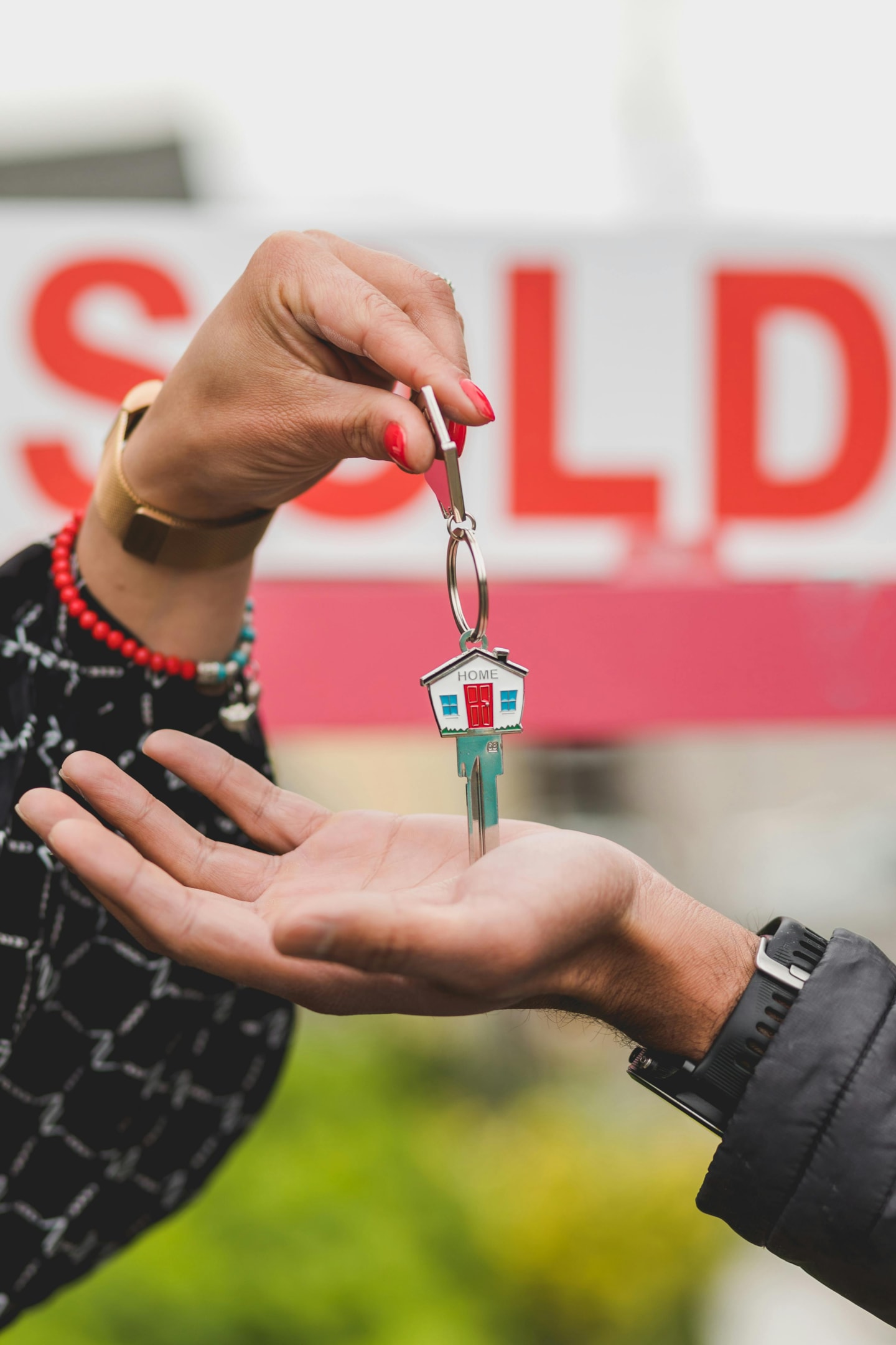 Keys being passed to home buyer in front of sold sign. 