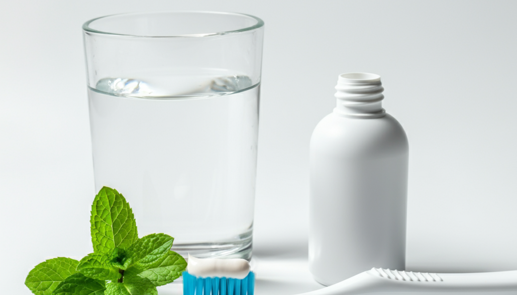 Tannbleking: Få hvitere tenner på en trygg måte 18 En tannbørste med tannkrem, et glass vann og friske mynteblader på en ren, hvit bakgrunn."