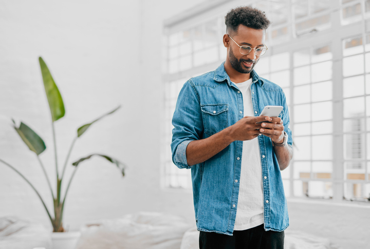 Young man in a blue denim shirt and glasses sending a text. 