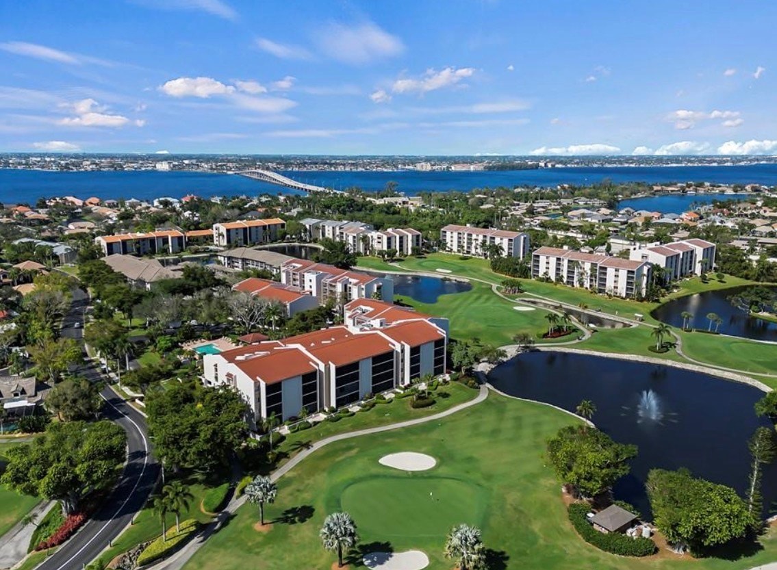 The image depicts a resort-style swimming pool surrounded by lush palm trees and comfortable lounge chairs, with a modern clubhouse building in the background. This inviting setting is part of the Landings community in Fort Myers, Florida, offering residents access to luxurious amenities and a vibrant lifestyle.