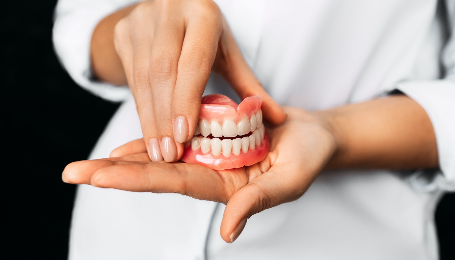 Tannlege holder en hel protese med begge hender, demonstrerer tannsett laget for pasienter med behov for tannprotese.