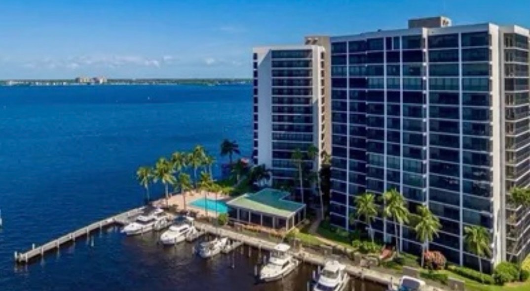 An aerial view showcases three luxury high-rise towers situated along the Caloosahatchee River in downtown Fort Myers, highlighting the impressive real estate development near Virginia Avenue. The scene captures the vibrant amenities and clubhouse, inviting potential buyers to explore the opportunities for sale in this picturesque location.