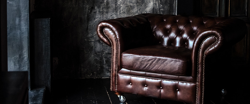 A brown natural leather armchair on castor wheels, in a black room. 