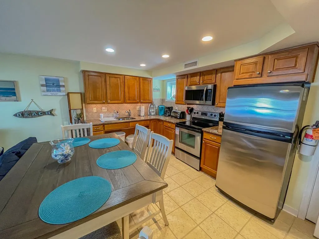 Modern kitchen and dining space inside Broadway Beach Condos Cape May unit featuring stainless steel appliances and wooden cabinets.