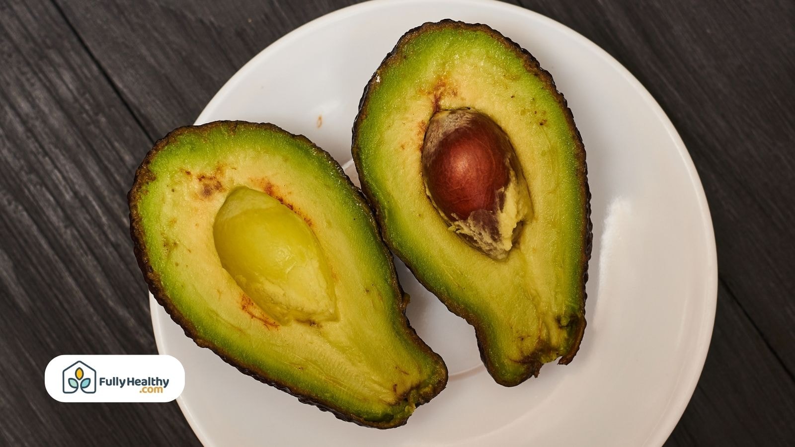 Halved avocado with pit on white round plate