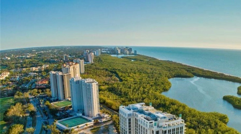 The image depicts luxury waterfront homes nestled along a pristine coastline, featuring white sand beaches and abundant natural light. This stunning scenery highlights the exclusive beachfront communities of Pelican Bay in Naples, FL, showcasing masterful coastal contemporary residences with beautifully designed outdoor spaces.