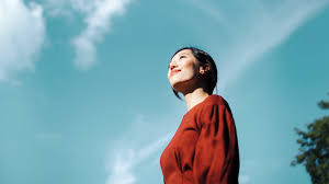 A woman in a red top looking up at the sky with a serene expression.