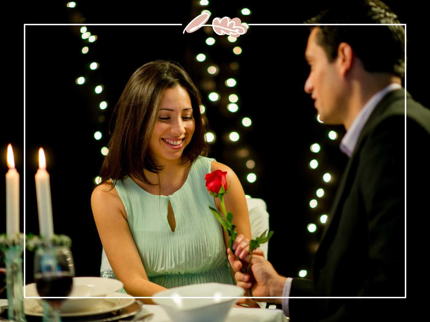 A man presenting a single red rose to a smiling woman during a candlelit dinner, capturing a moment of romance - Fabulous Flowers and Gifts.