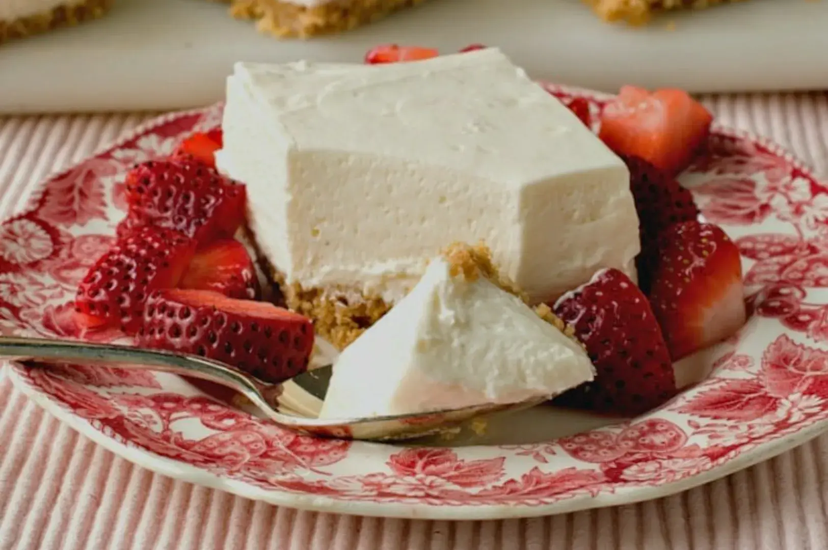A slice of cheesecake on a decorative plate, garnished with fresh strawberries and a fork.