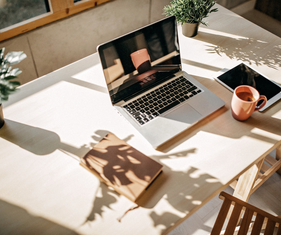 a desk with wooden chair, journal, laptop, tablet, and orange mug