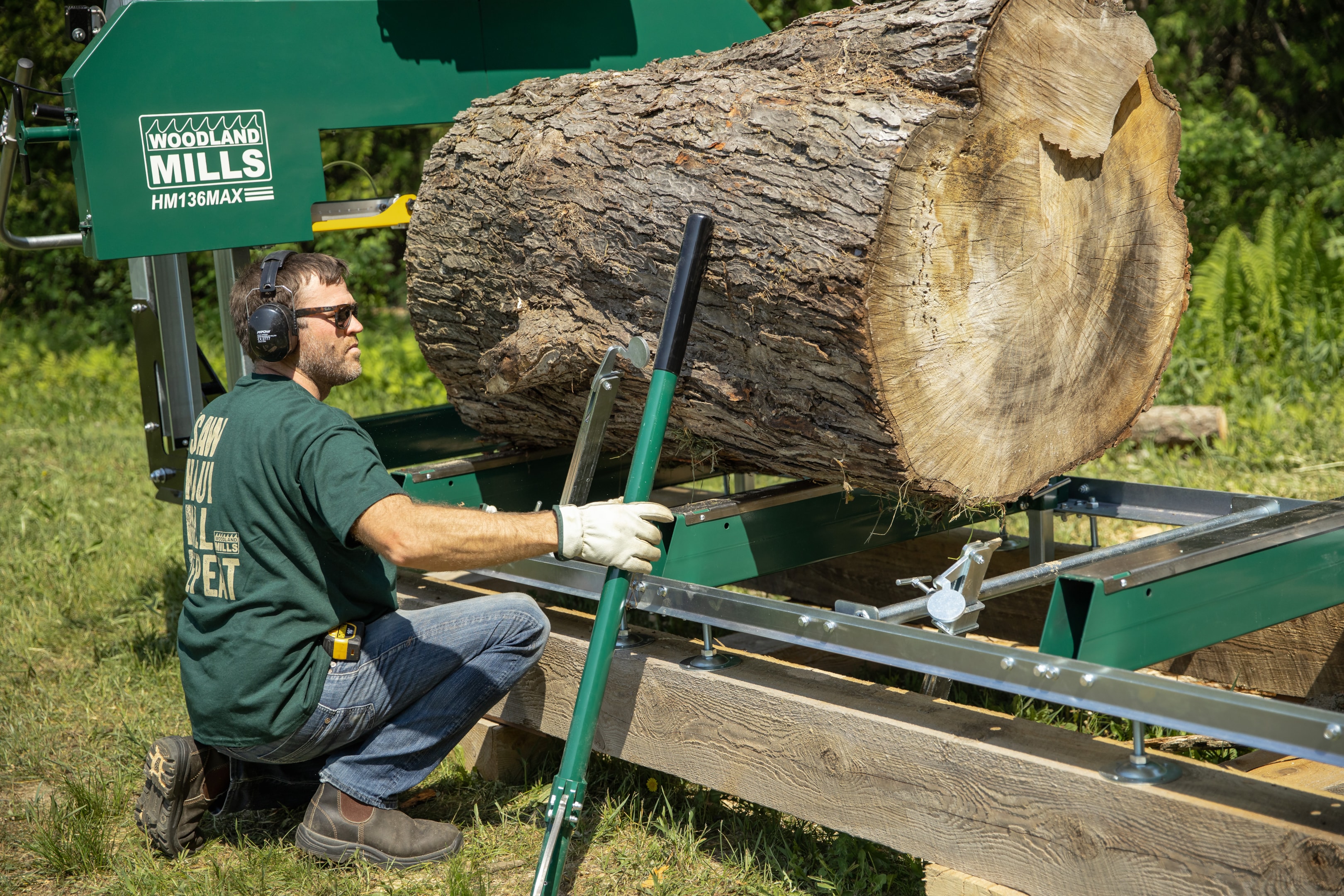 A portable sawmill owner resting a cant hook against a log.
