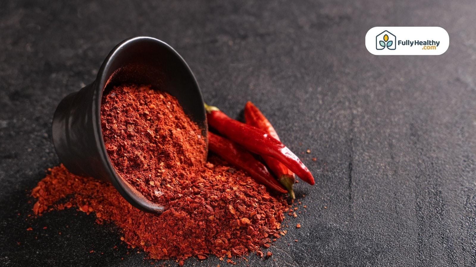 Spilled black bowl of crushed chili with whole chilies beside it