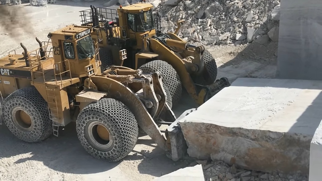 Two large yellow Caterpillar wheel loaders working in a quarry, moving a large block of white marble