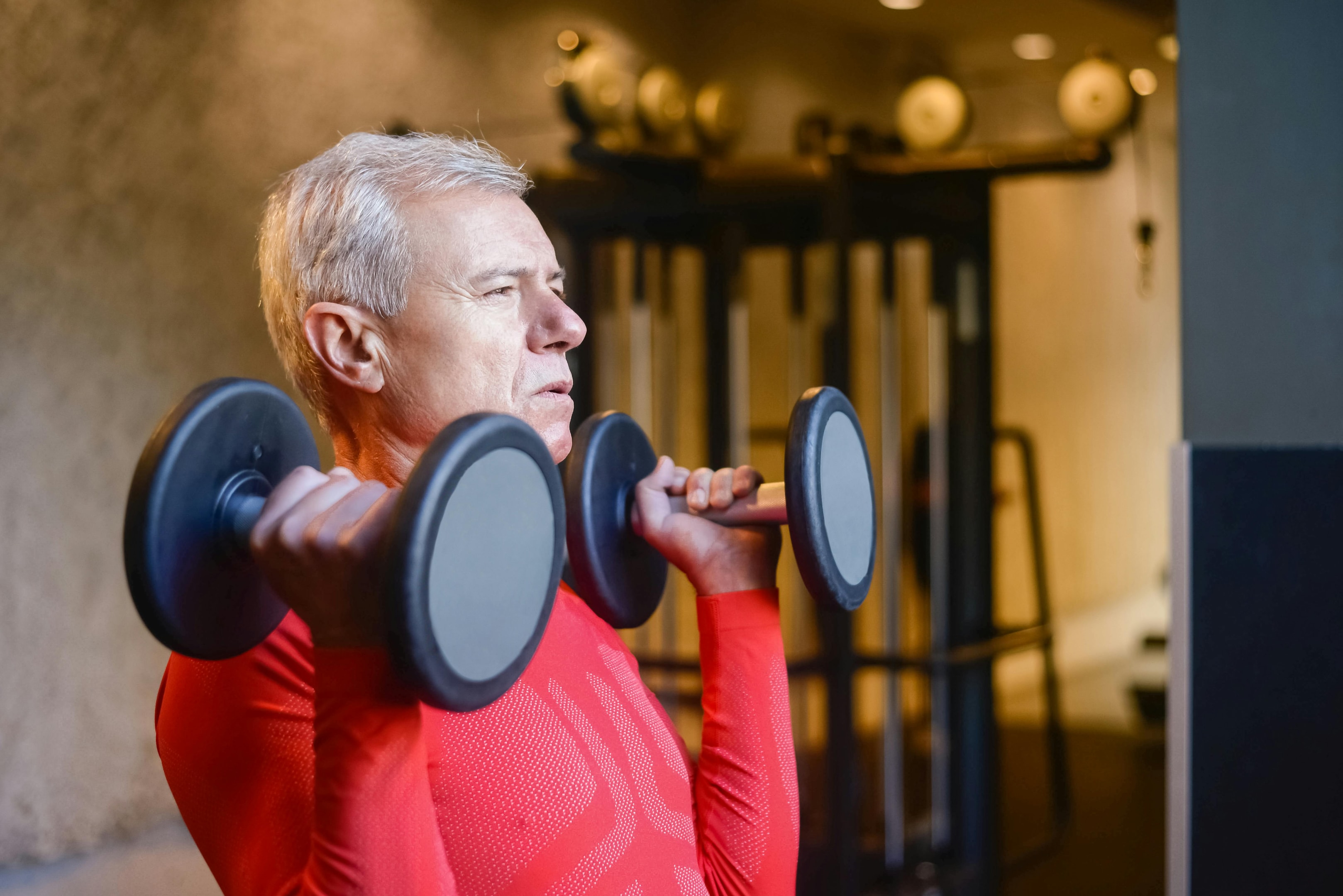 The right equipment significantly impacts the safety and effectiveness of your workouts. Resistance bands like the OmniBand Pro are portable and great for low-impact workouts, ideal for older adults. They can increase resistance up to 150 pounds, providing a versatile option for various exercises.  Dumbbell sets with neoprene coating offer easy gripping, making them ideal for maintaining strength. Stability balls can improve balance and strength and often come with user-friendly exercise instructions, benefiting seniors.  Under-desk exercise bikes promote movement while sitting, eliminating the need for prolonged standing. Elliptical machines provide a low-impact workout, reducing joint strain while offering cardiovascular benefits.  Foam rollers aid muscle recovery and improve flexibility, making them useful for post-exercise routines. The right equipment helps create an effective and safe exercise program tailored to your needs.  Starting Slow and Progressing Gradually  When beginning a new exercise routine, start slow and progress gradually. Push yourself enough to feel your muscles engaging. Avoid any pain or exhaustion. If you experience joint pain during exercise, back off to avoid further strain.  Warm up and cool down with easy walking or gentle stretching. This prepares your body for exercise and aids in post-workout recovery.  Starting slow and increasing intensity gradually helps build a sustainable, effective routine that aligns with your fitness goals. Photo by Kampus Production: https://www.pexels.com/photo/elderly-man-lifting-dumbbells-6922181/