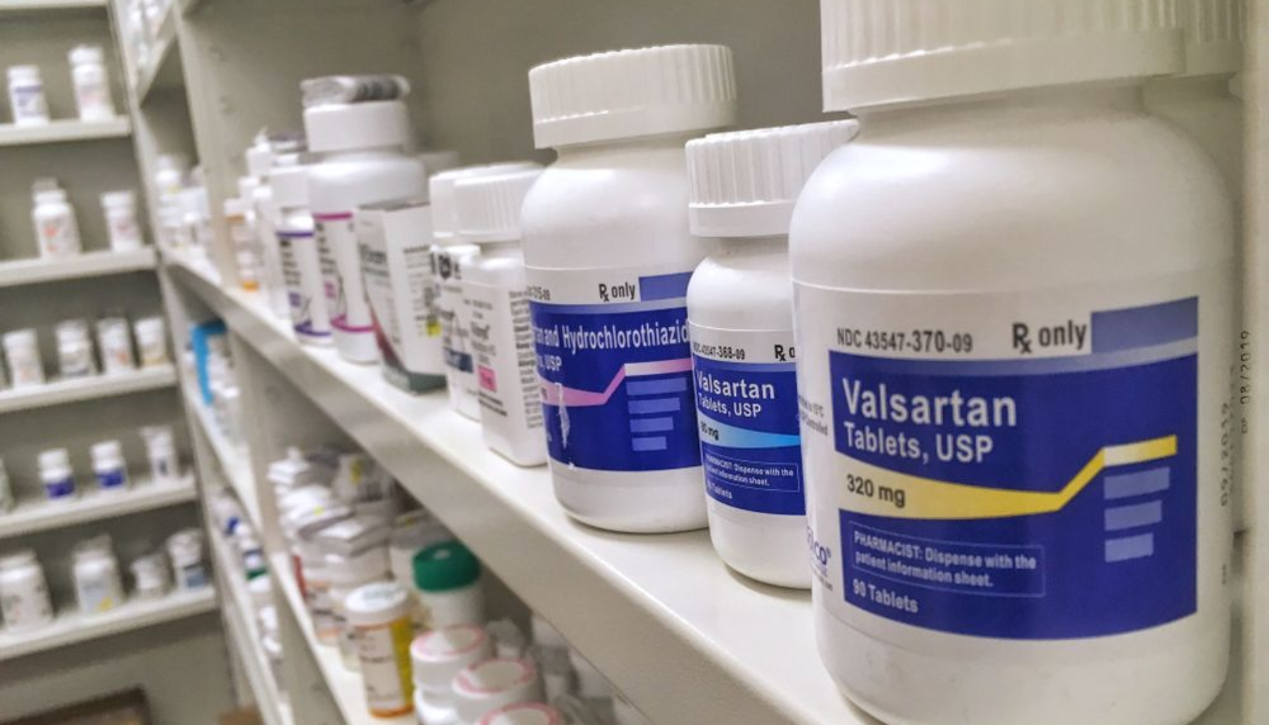 Bildet viser flere legemiddelbokser på et apotekshylle, hvor en av de mest fremtredende er merket Valsartan Tablets, USP 320 mg. Valsartan brukes ofte til behandling av høyt blodtrykk og hjertesvikt, samt for å redusere risikoen for komplikasjoner etter hjerteinfarkt.