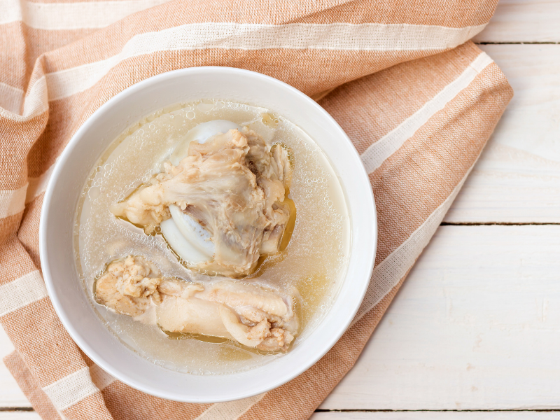 An image showing a bowl of bone broth with animal bones and herbs, rich in the amino acid glycine.