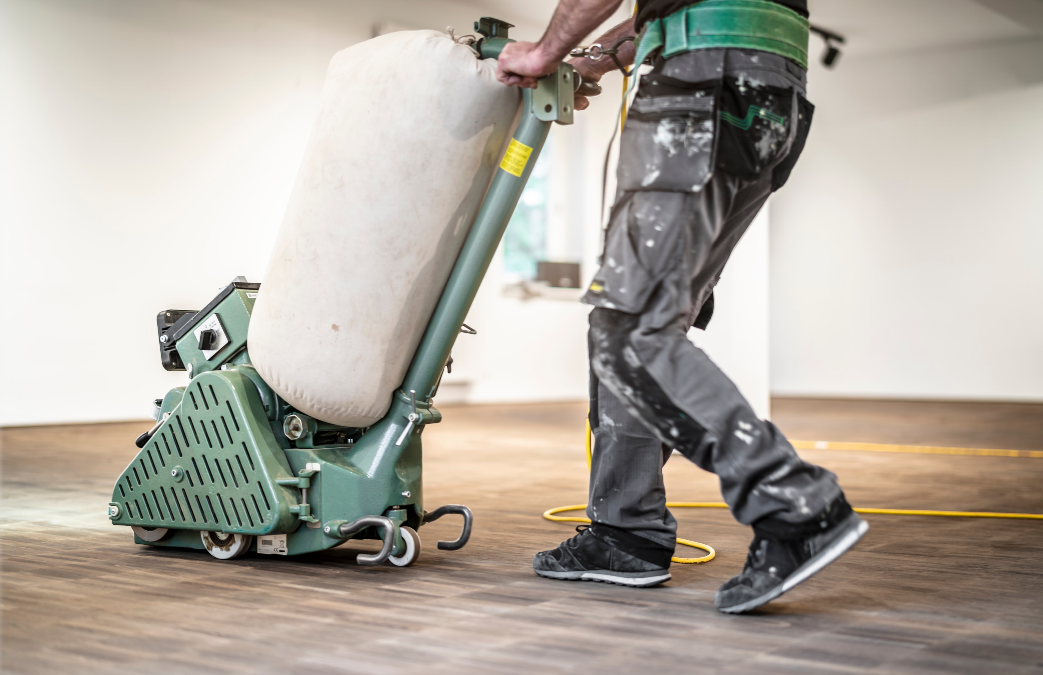 Handwerker schleift die Parkettoberfläche mit einer professionellen Maschine – eine Szene, die zeigt, wie fachkundige Hilfe dabei unterstützt, beschädigte Stellen zu renovieren und wieder etwas Glück und Natürlichkeit auf die Seite des Holzbodens zu bringen.